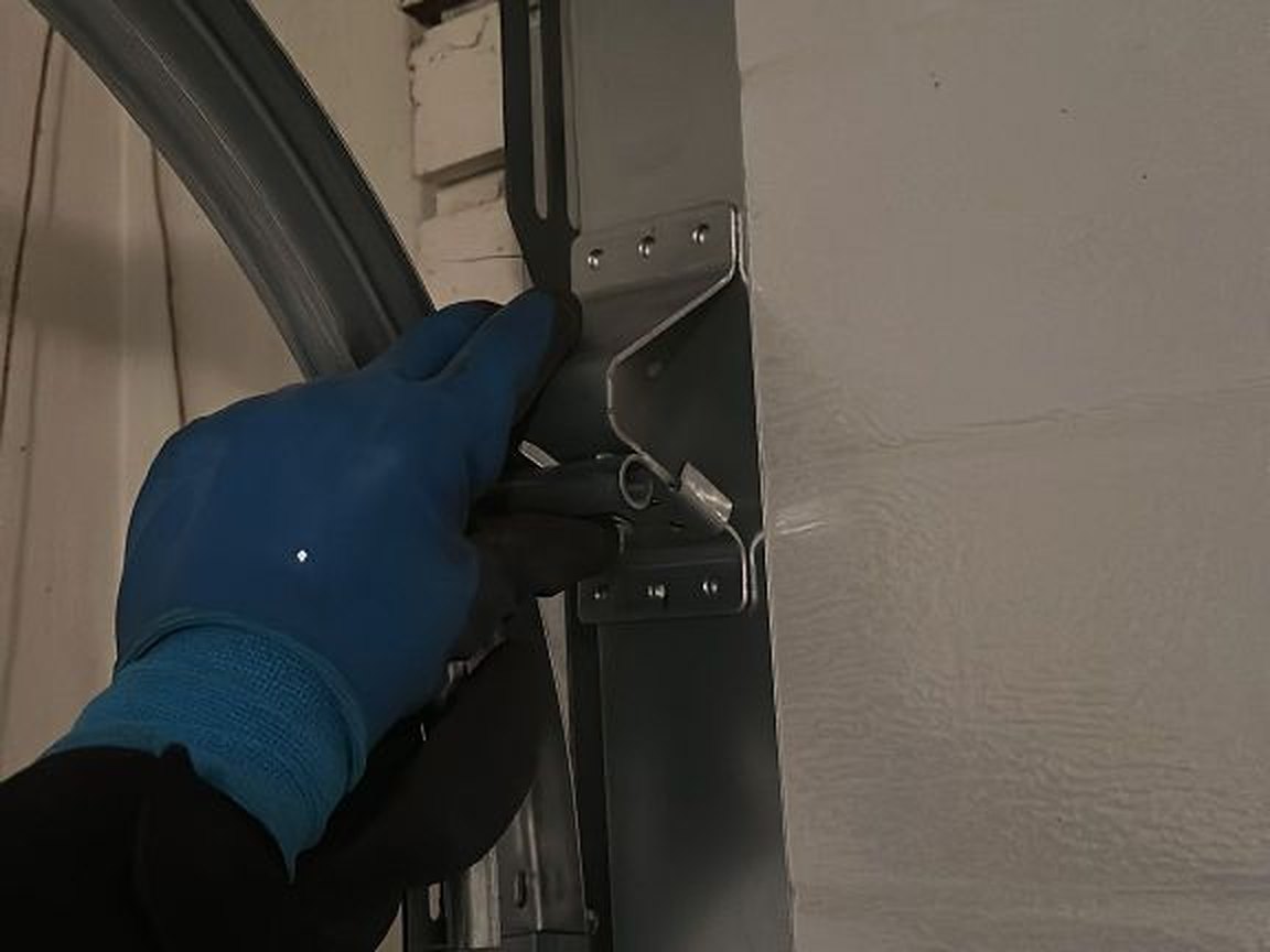 Gloved hand steadying the curved track at the flag bracket during a maintenance visit